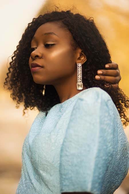 Black womxn with a professional curly afro divided hairstyle wearing a light blue top and golden earrings