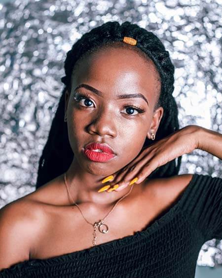 Black womxn with a professional yarn braids hairstyle standing in front of a shiny background