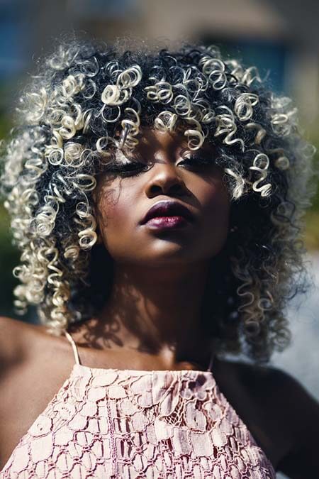 Black womxn with a professional short-mid length curly hair with highlights hairstyle, looking to the camera