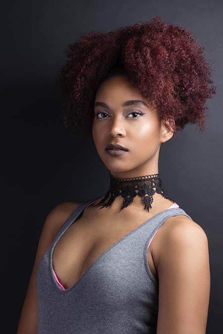Black womxn with a professional afro-textured puff dyed purple/red hairstyle with the puff falling to the front side of the head