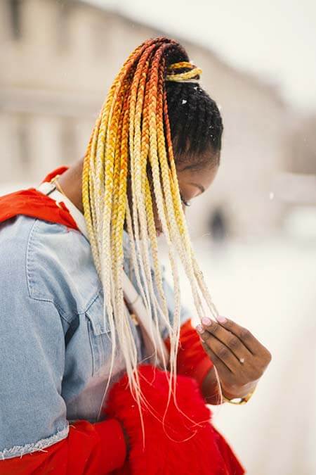 Black womxn with a professional long ombre black-orange-yellow-blonde dreadlocks hairstyle tied in a ponytail covering her face with it