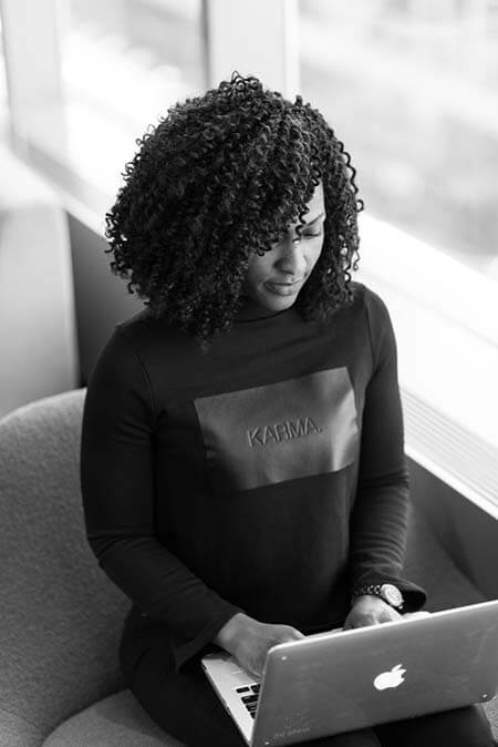 Black womxn with a professional mid 3B afro hairstyle sitting with a laptop on her lap and typing