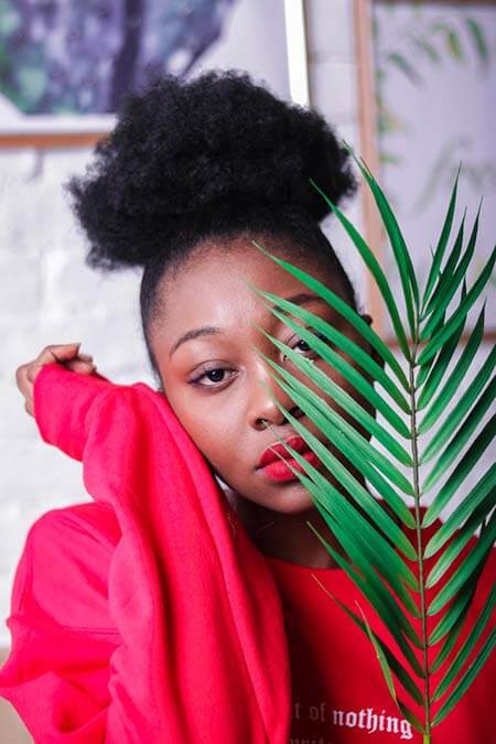 Black womxn with a professional afro-textured puff hairstyle, wearing a red sweater standing in front of a white brick wall