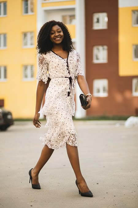 Black womxn with a professional mid 3B afro hairstyle smiling to the camera and walking in front of a building