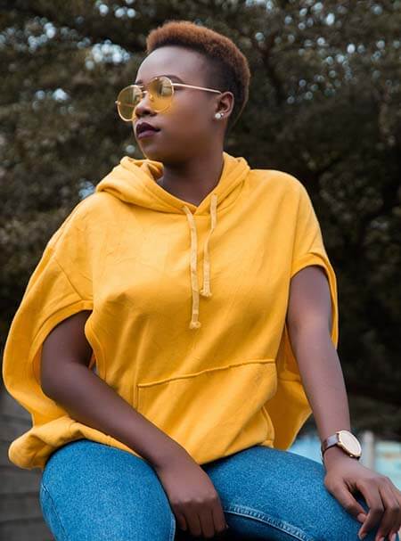 Black womxn with a professional short TWA dyed light brown hairstyle with shaved sides sitting on a wooden deck