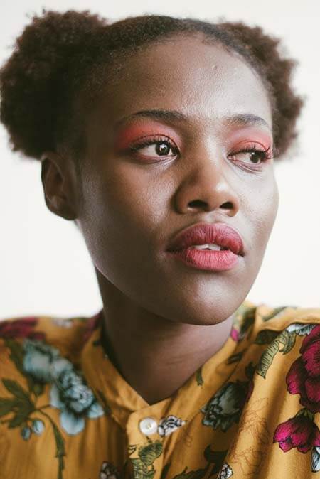 Black womxn looking to the side with light red eye make up and professional 2-bun afro-textured puffs hairstyle