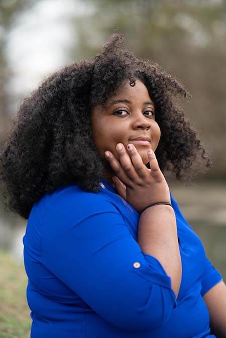 Black womxn with a professional 3B afro hairstyle wearing a blue shirt looking to the camera