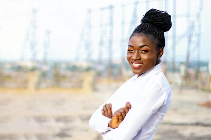 Black womxn with a professional nubian twists gathered in a high bun hairstyle has her arms crossed and smiling