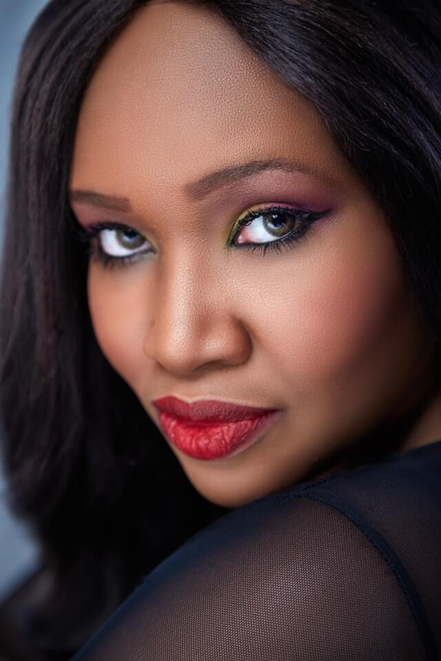 Black womxn with workplace makeup, bright red lipstick, black eyeliner, yellow and pink eyeshadow, looking to the camera