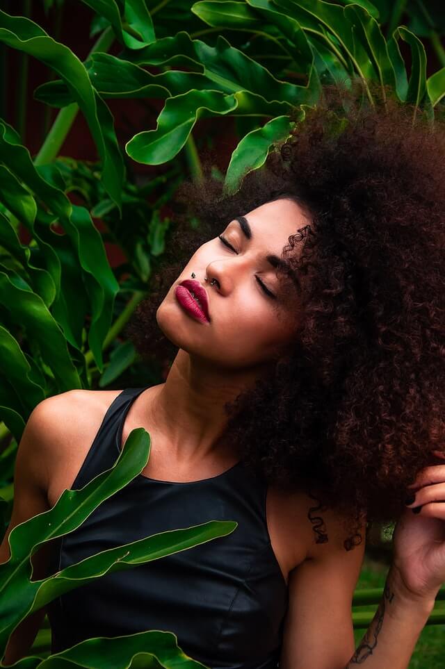Black womxn with professional big afro, workplace makeup, red lipstick, holding her head up to the side with closed eyes
