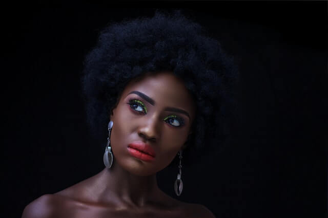 Black womxn with professional short afro, workplace makeup, coral lipstick and golden eyeshadow, looking up to the side