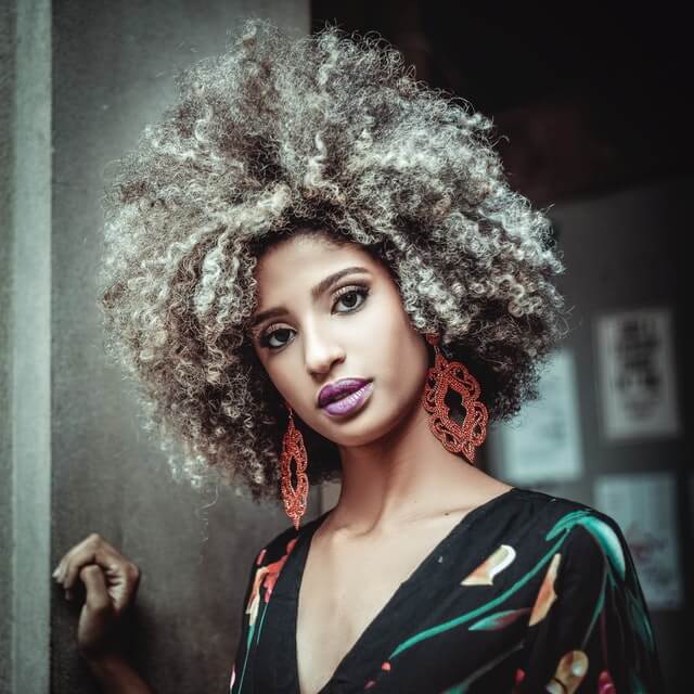 Black womxn with professional big afro with highlights, purple lipstick and big orange earrings, looking to the camera