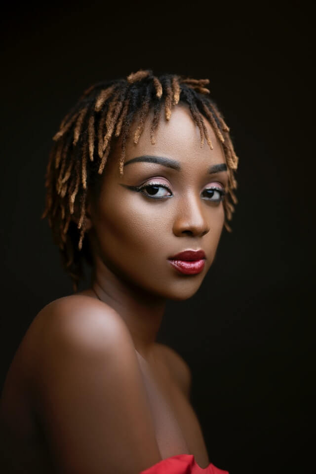 Black womxn with professional short locs with blonde highlights, red lipstick and eyeliner, looking to the camera